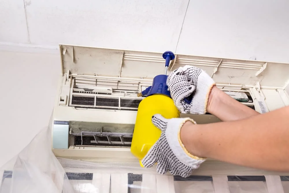Technician applying antimicrobial spray to a wall-mounted AC unit for residential mold remediation in Charlotte, NC.