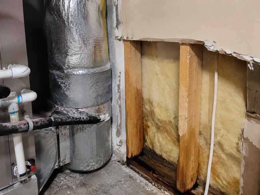 HVAC ductwork beside an opened wall cavity showing damp insulation and moisture buildup from condensation near the wall framing.